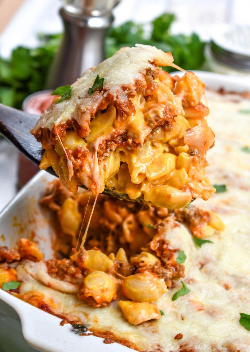 ingredients for lasagna mac and cheese laid out on a wooden table, including pasta, cheese, ground beef, and tomato sauce