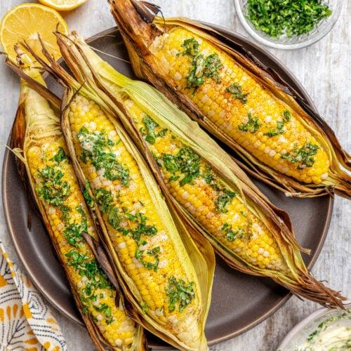 overhead shot of a platter of grilled corn with cinnamon-maple butter, garnished with chopped parsley