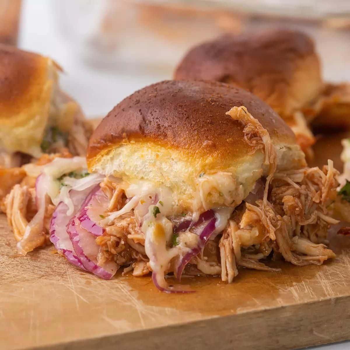 close-up of cherry-cola bbq chicken sliders on a rustic wooden board