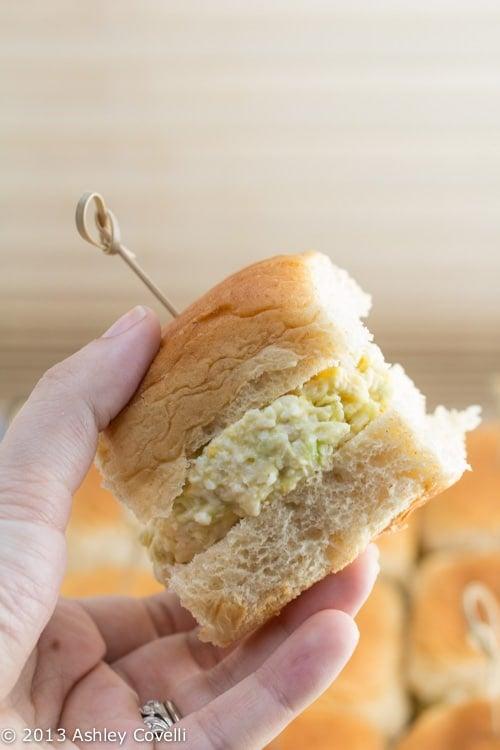 a hand placing a scoop of chicken salad onto a cut Hawaiian roll