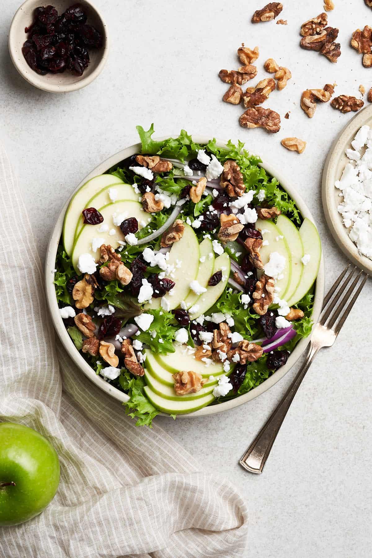 Apple walnut salad served in a clear bowl on a dining table with other light dishes
