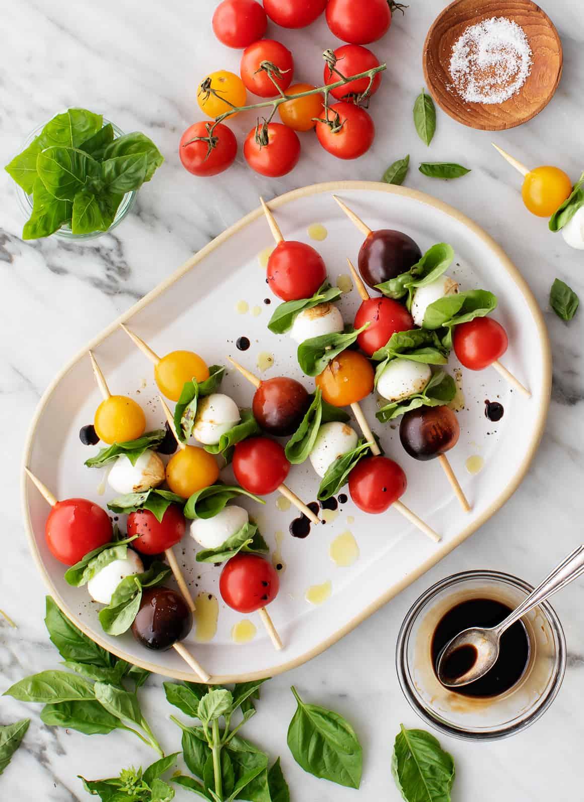 Ingredients for caprese skewers: cherry tomatoes, mozzarella balls, basil leaves, balsamic vinegar
