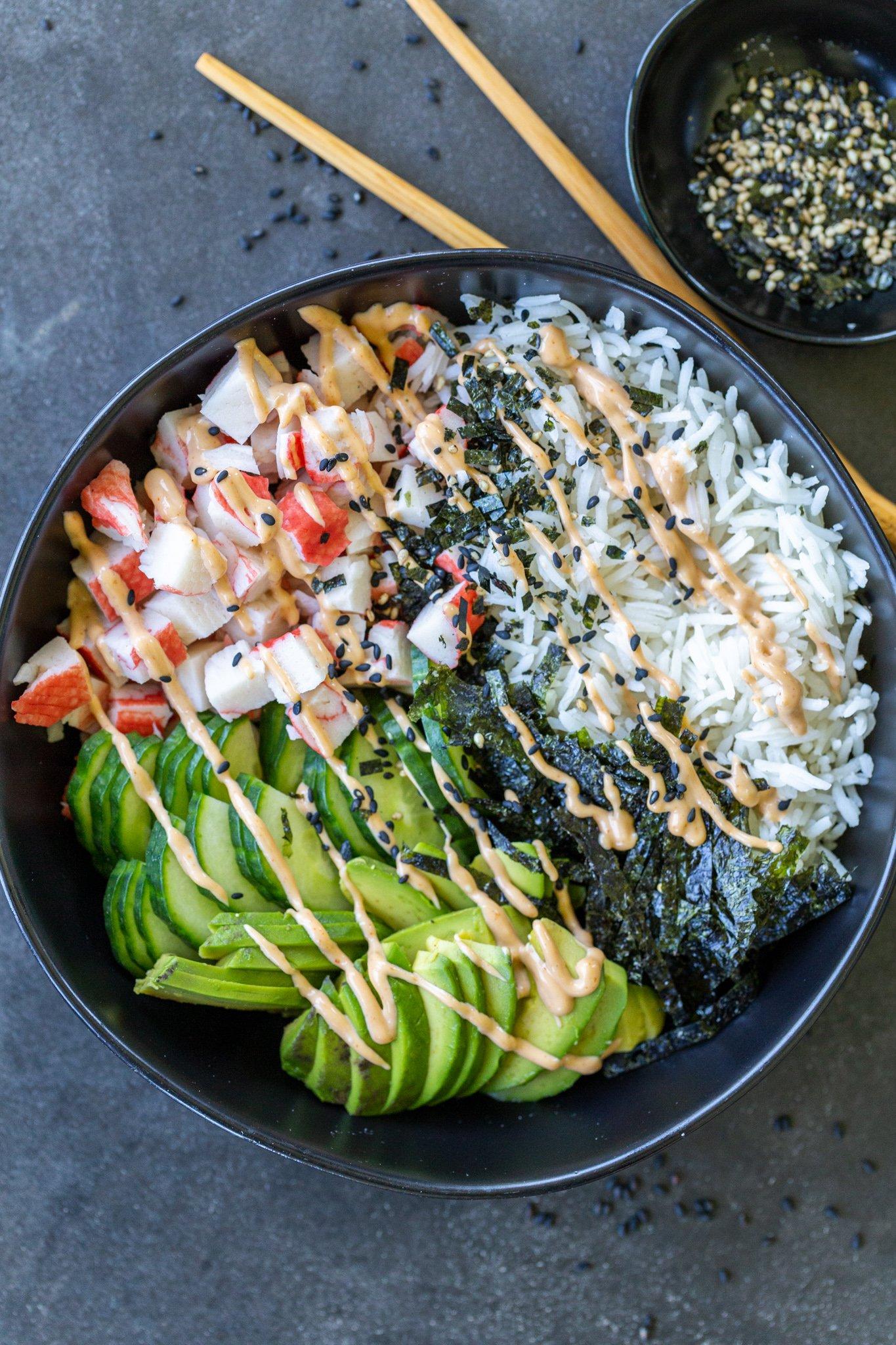 A person arranging avocado slices on a sushi bowl