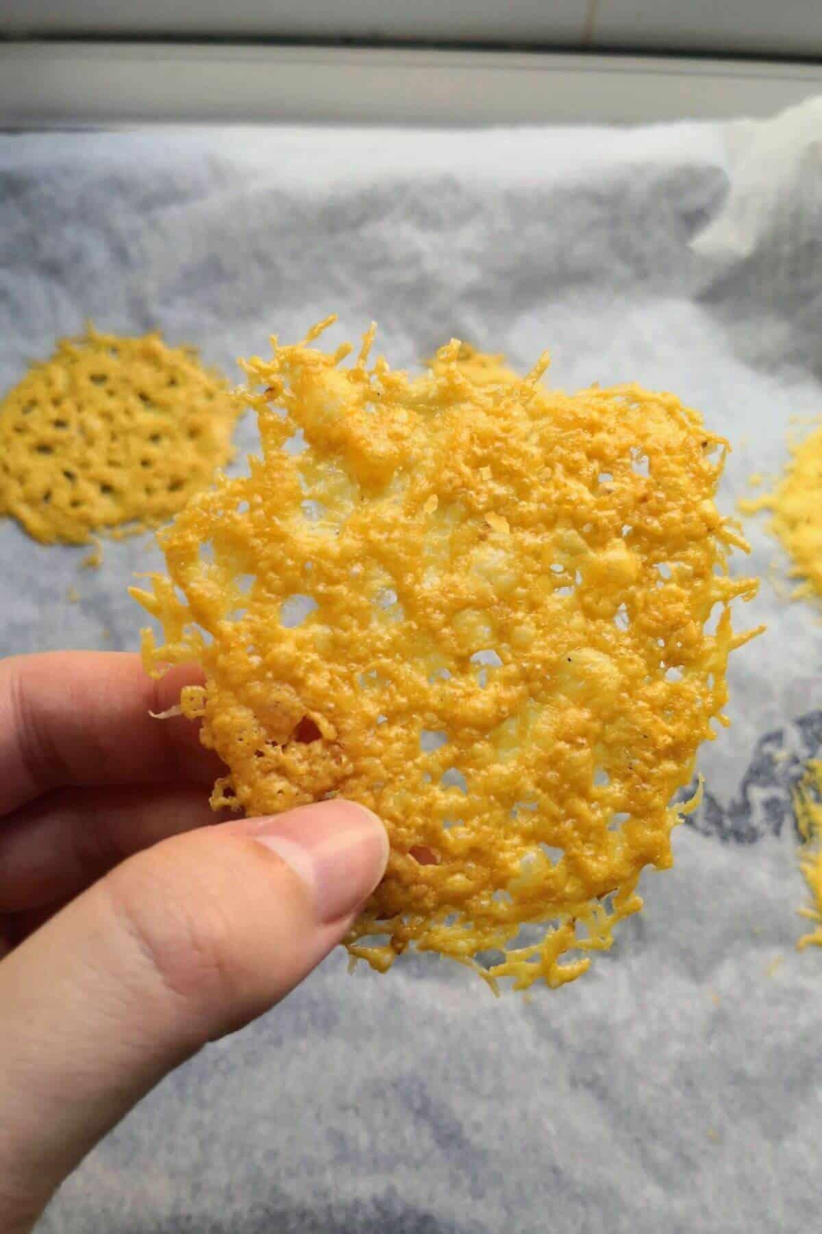Close-up of a hand reaching for a crispy baked parmesan bite on a wooden board