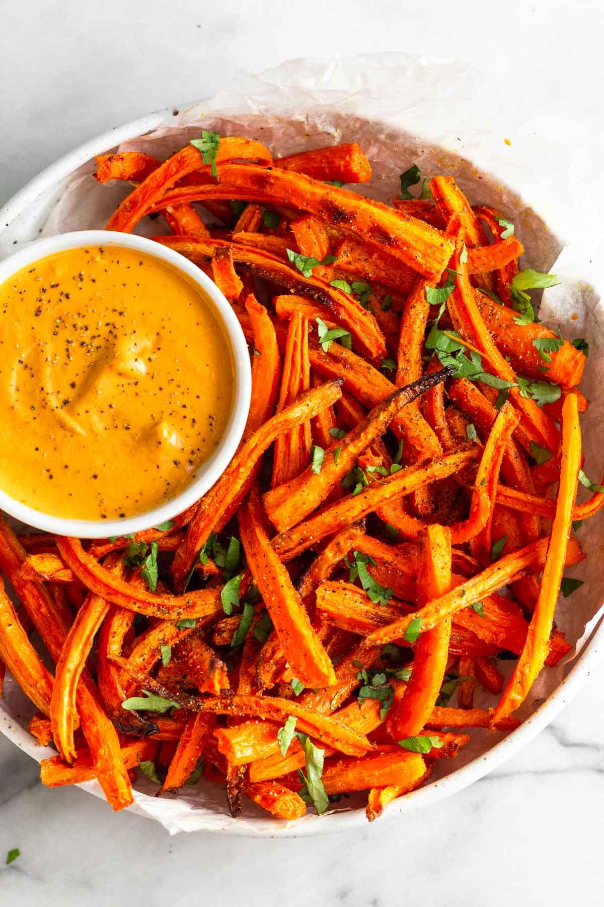 a bowl of curried carrot fries next to a small bowl of yogurt dip, garnished with fresh cilantro