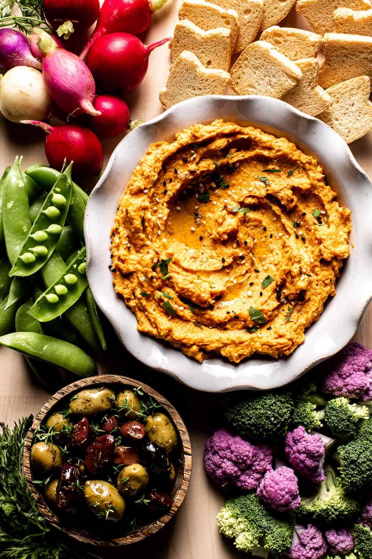 close up shot of carrot and ginger hummus with crackers and vegetables