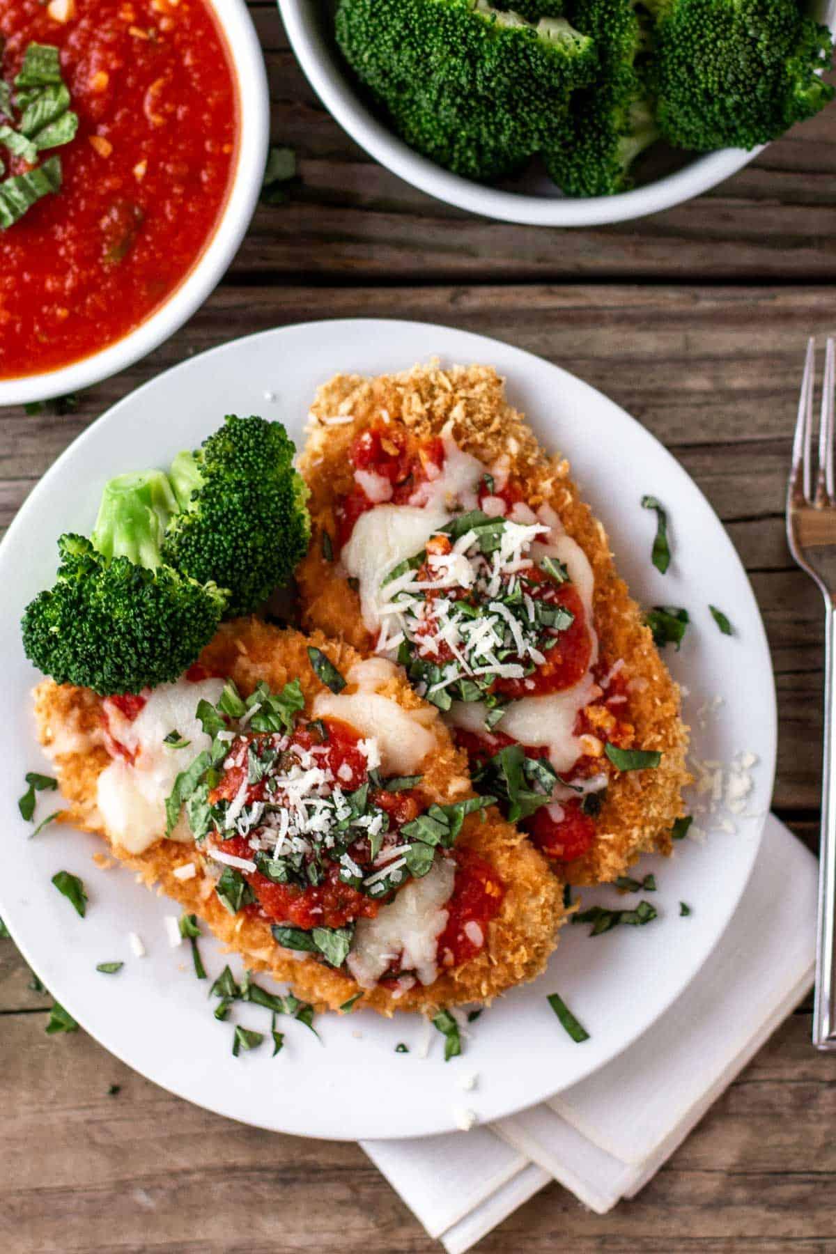 Mediterranean Chicken Parmesan plated with a side of pasta and a fresh salad