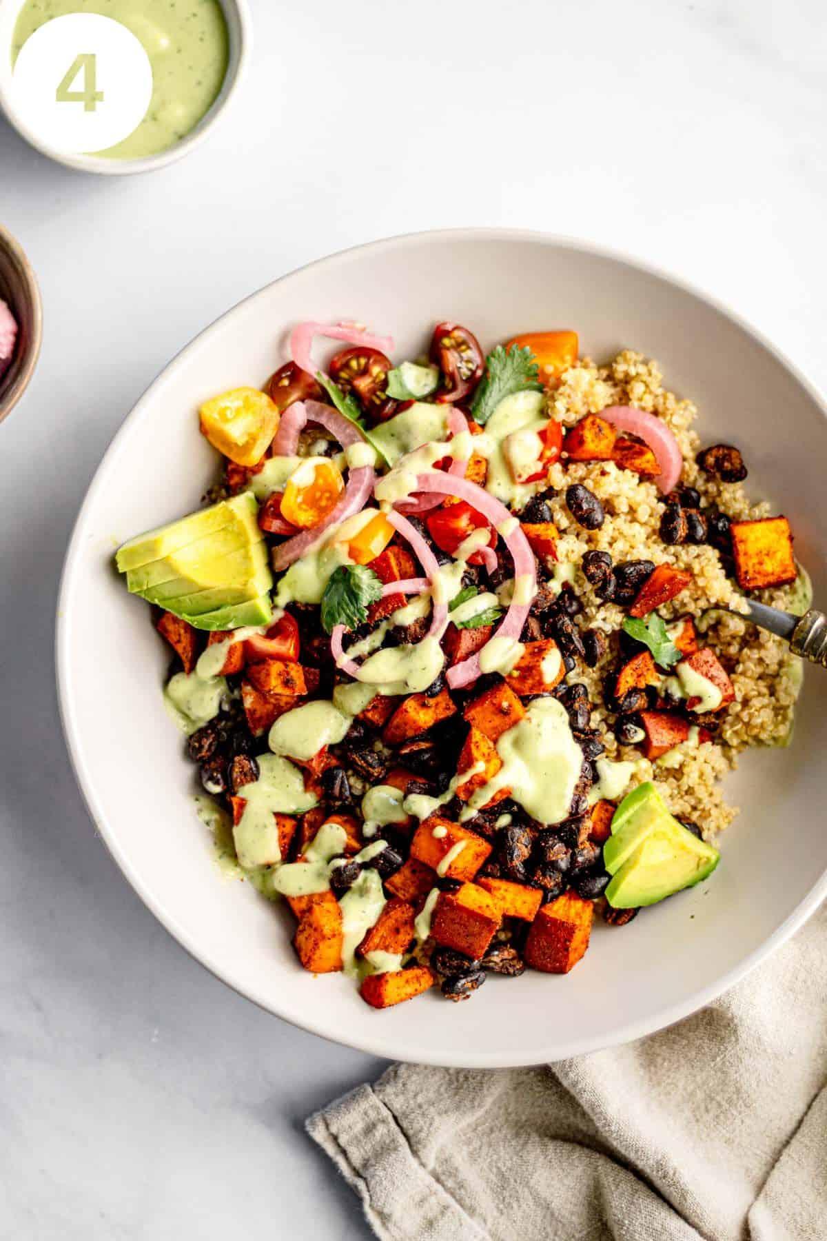 A person adding toppings to a black bean sweet potato quinoa bowl