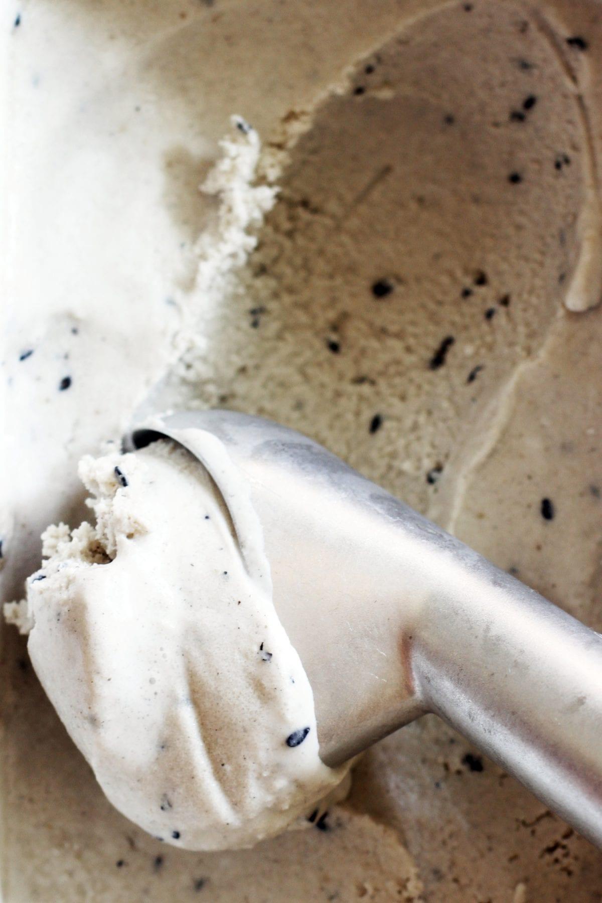 a person scooping black sesame lavender frozen yogurt into a bowl