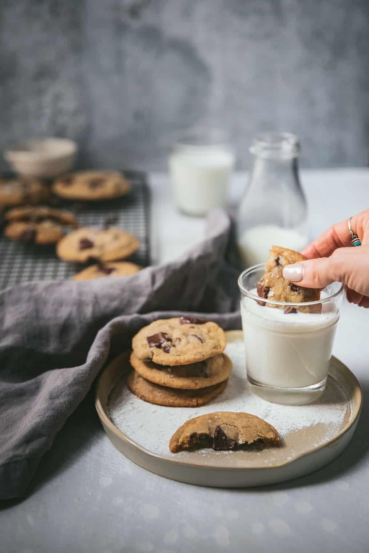 Warm chewy brown butter cookies stacked on a plate with a glass of milk, rustic kitchen background