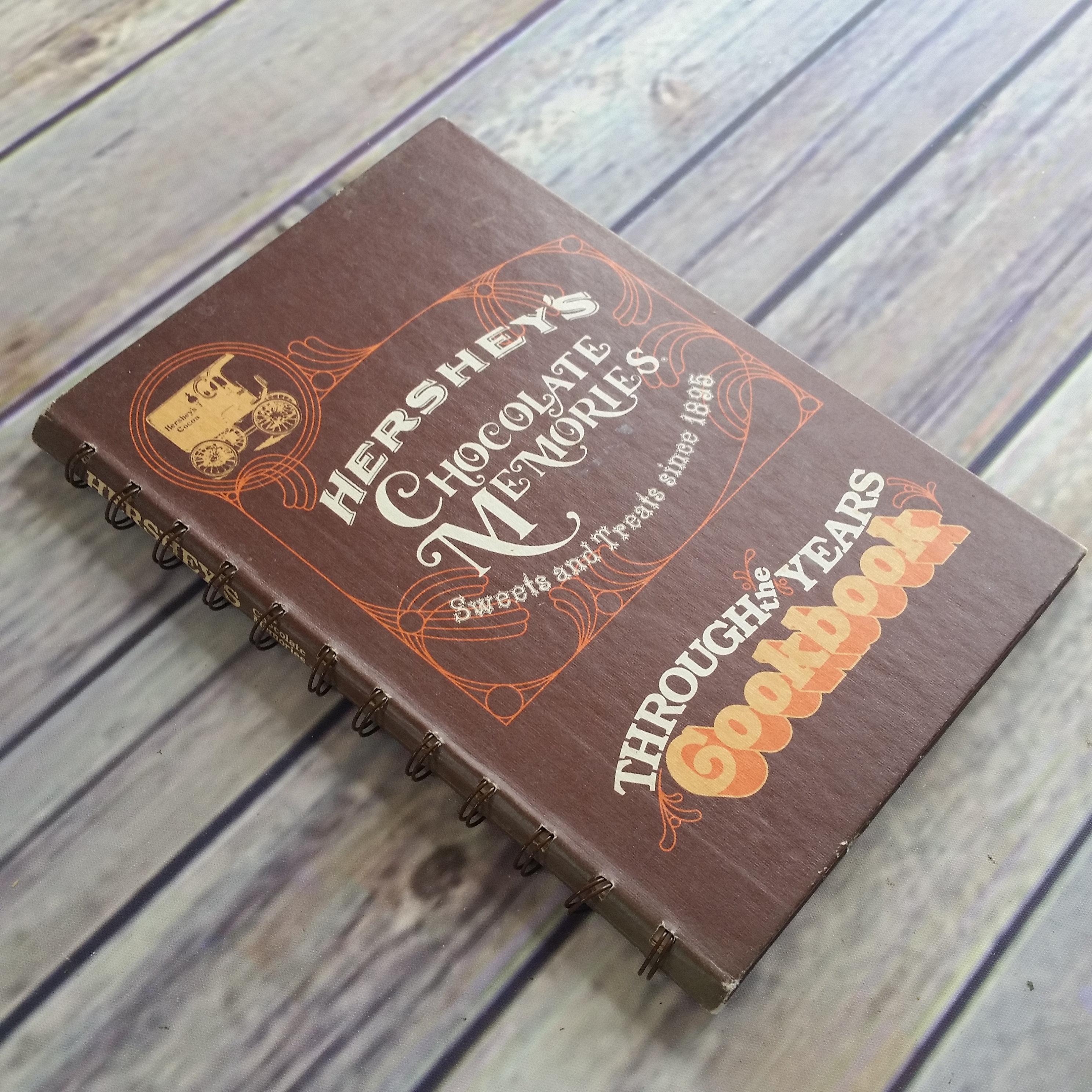 Vintage cookbook open to a chocolate recipe, with handwritten notes and a glass of bourbon in the background