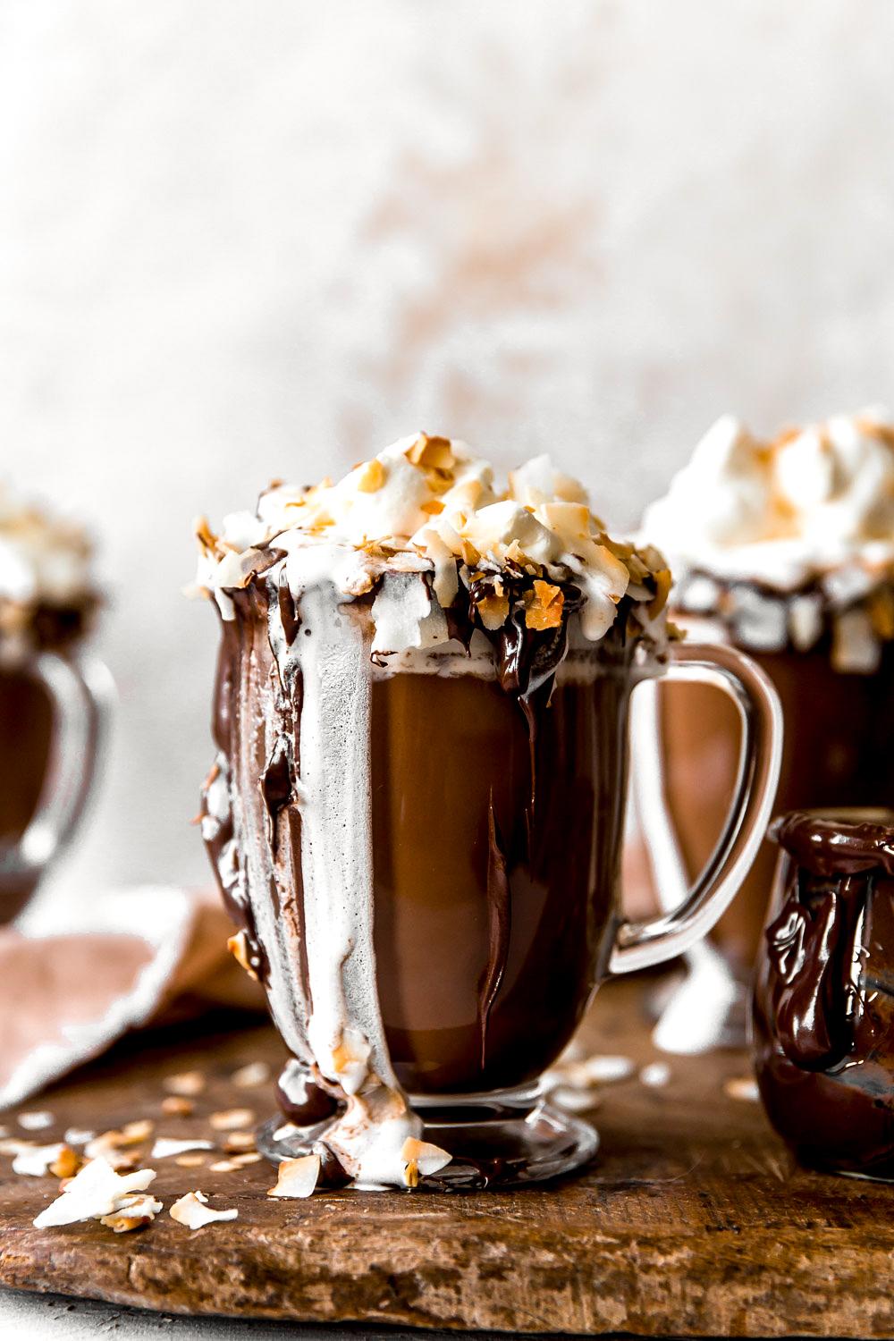 steaming mug of coconut hot chocolate with coconut whipped cream and toasted coconut flakes, tropical background, cozy setting