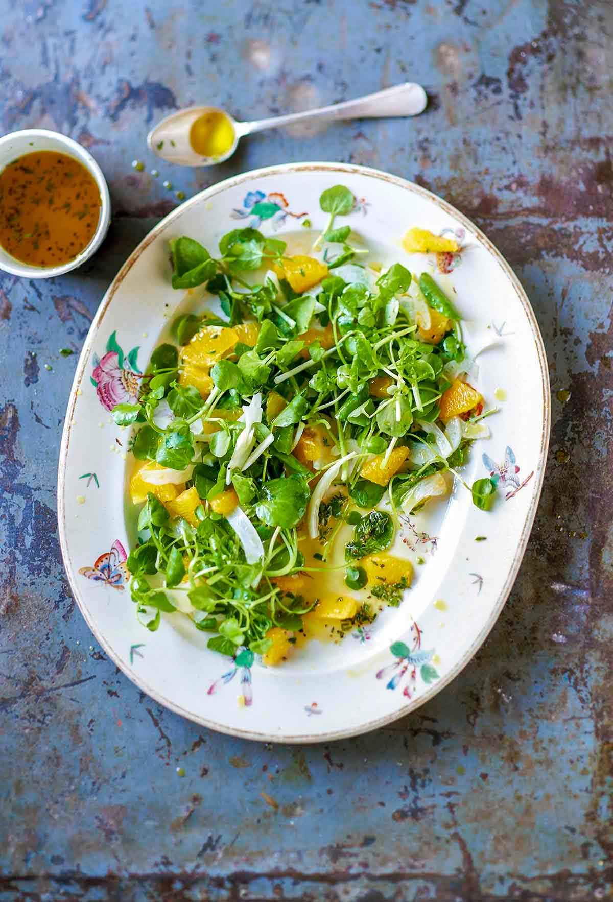 Overhead shot of the completed watercress and orange salad with optional toppings like nuts and cheese arranged around it.