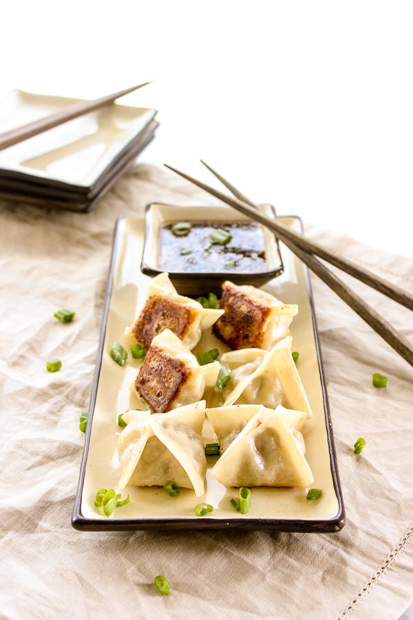 An overhead shot of a plate of pulled pork potstickers with soy ginger glaze, garnished with sesame seeds and green onions, set on a rustic wooden table.