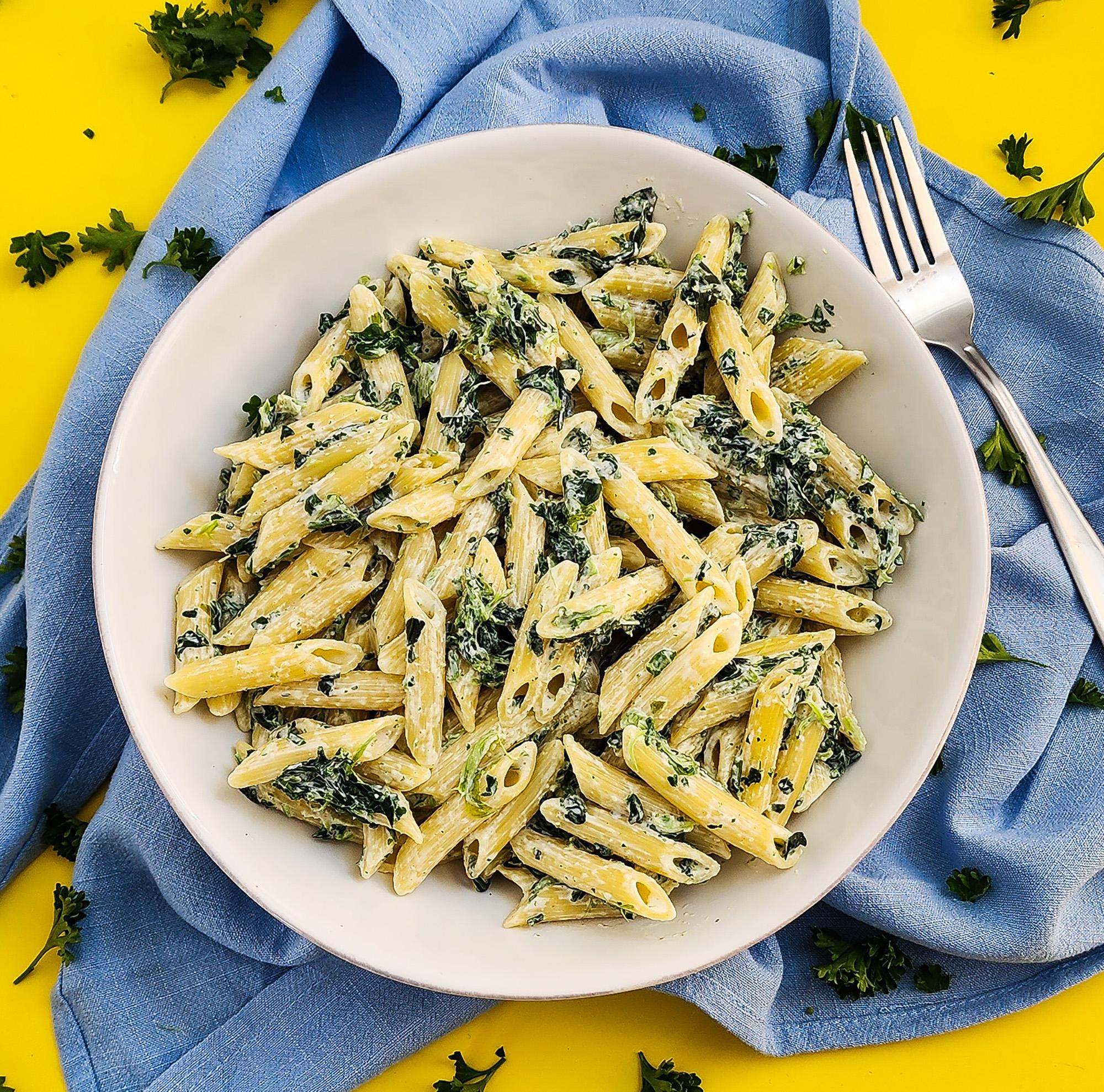 ingredients for creamy garlic spinach pasta laid out on a wooden cutting board, including fresh spinach, garlic, heavy cream, pasta