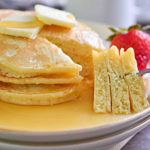 Pancakes on a plate, one with a fork cutting into it, revealing fluffy texture