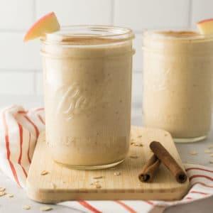 Spiced Apple Pie Milkshake with apple slices and cinnamon sticks on a wooden board