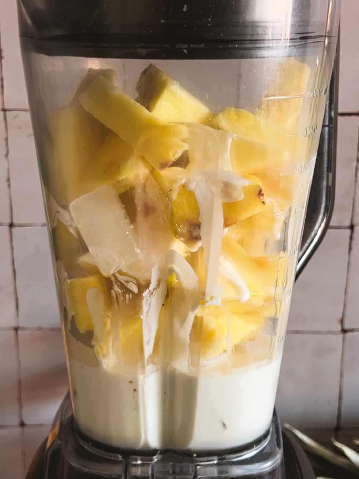 person blending a pineapple coconut protein smoothie in a high-speed blender