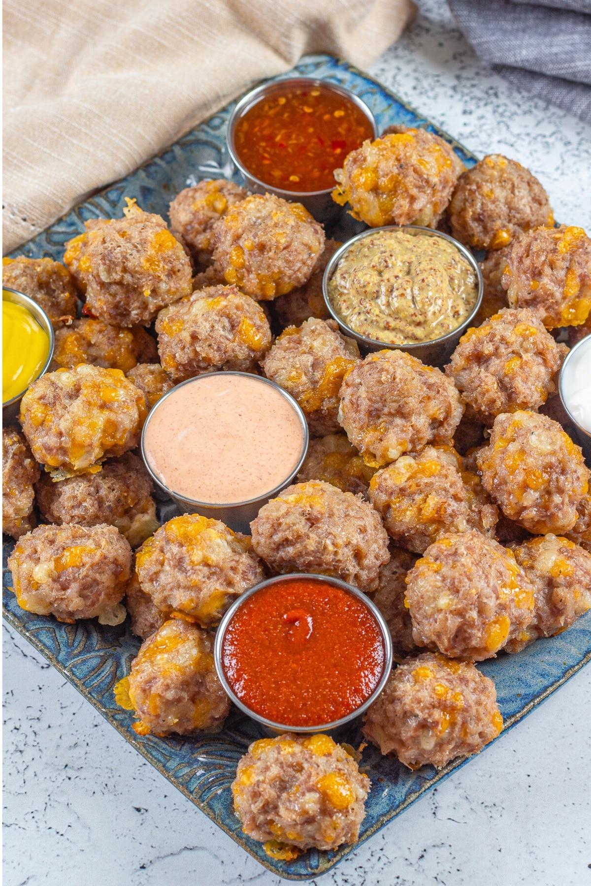 Ingredients for maple heat sausage balls laid out: ground sausage, shredded cheddar, biscuit mix, maple syrup, hot sauce, butter