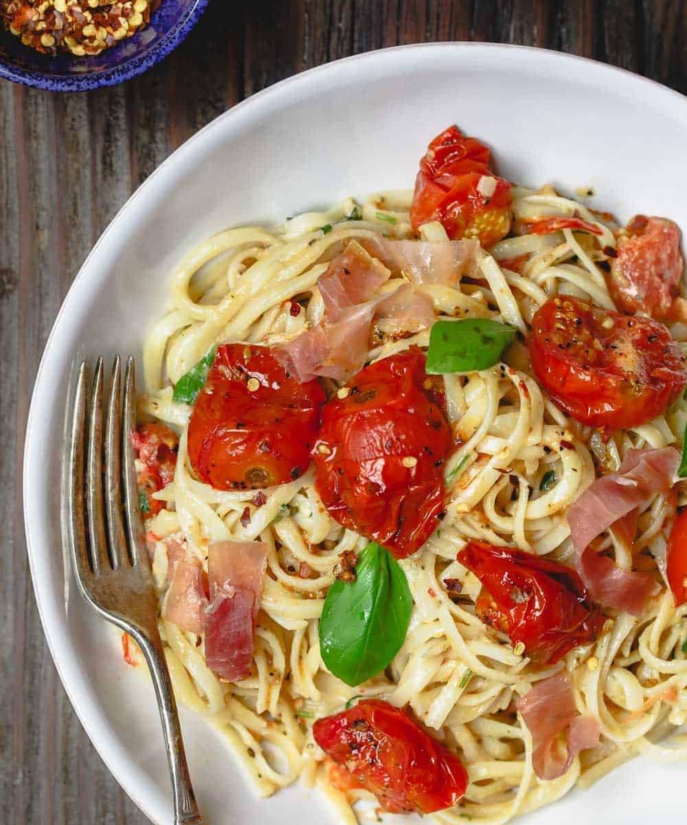 a fork twirling carbonara with roasted tomatoes and basil, showcasing the creamy sauce