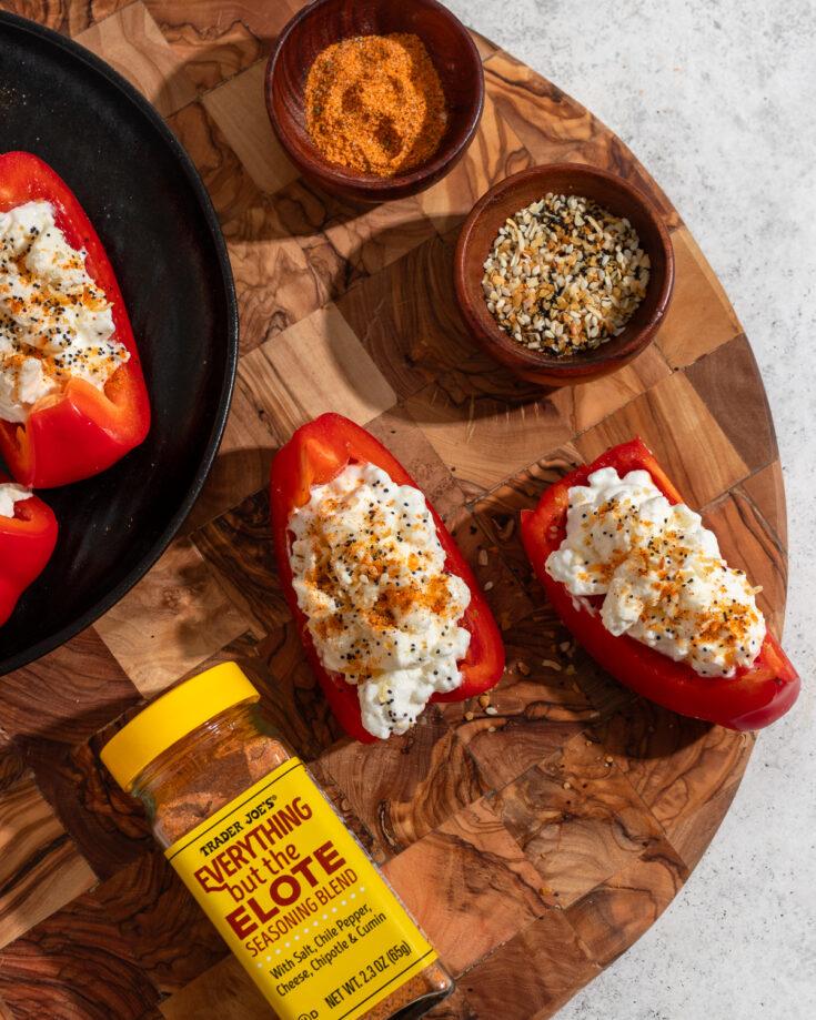 A hand placing shredded cheese on top of stuffed peppers