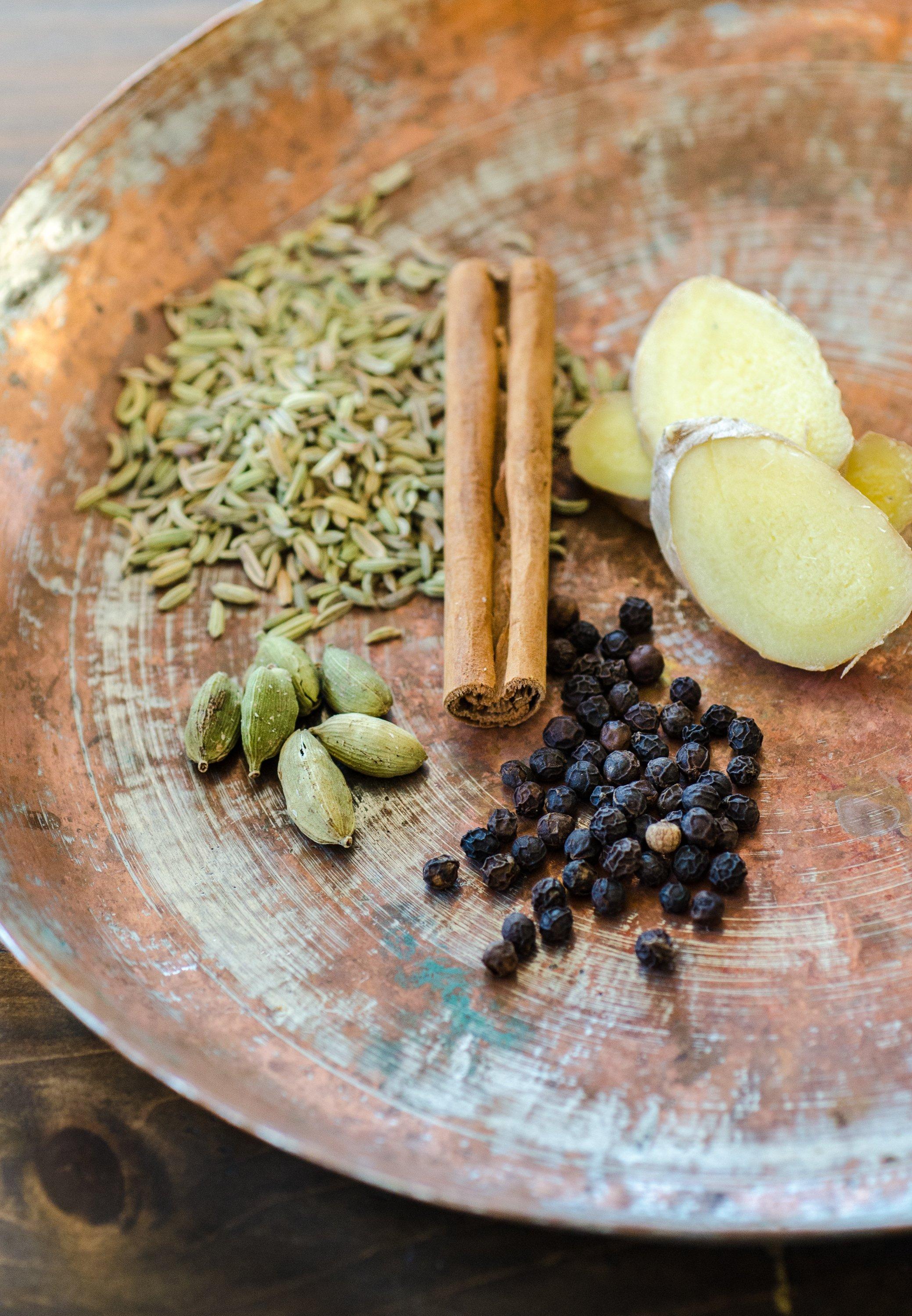 overhead shot of chai spices (cinnamon sticks, cardamom pods, cloves, ginger) scattered on a wooden surface with marshmallows