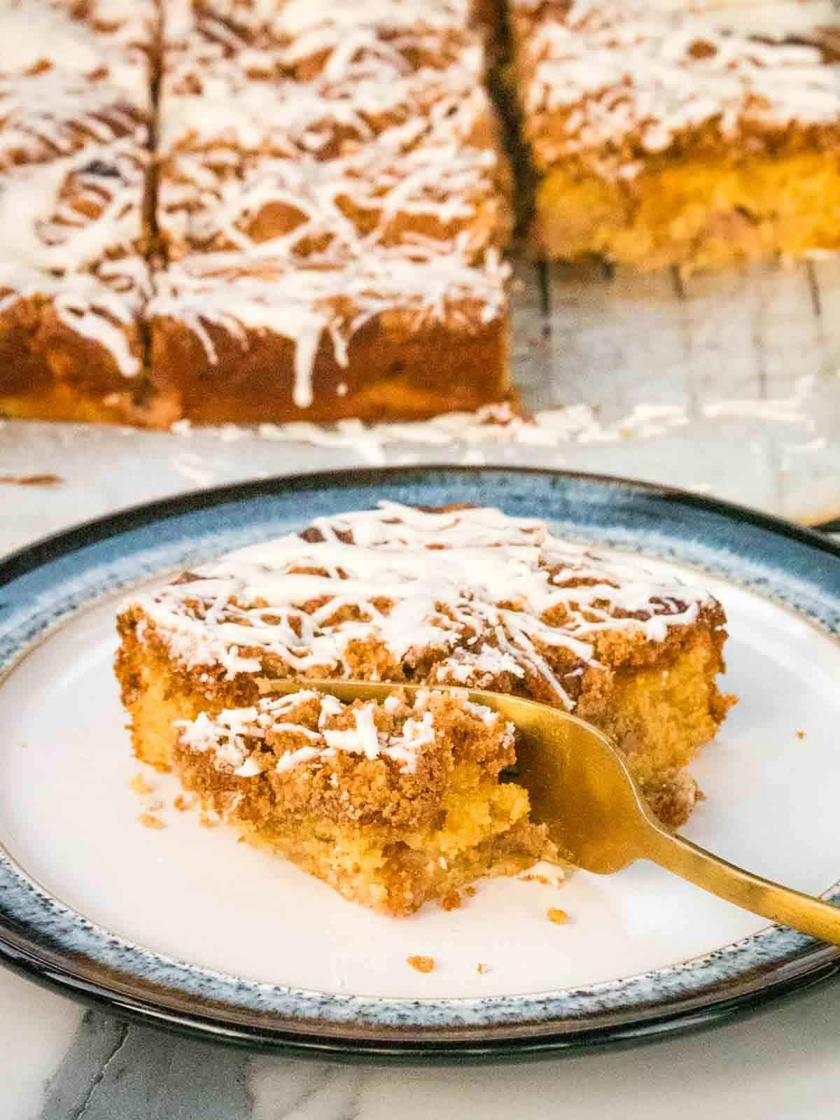 slice of spiced rhubarb crumble cake served on a plate, with a fork and a cup of tea