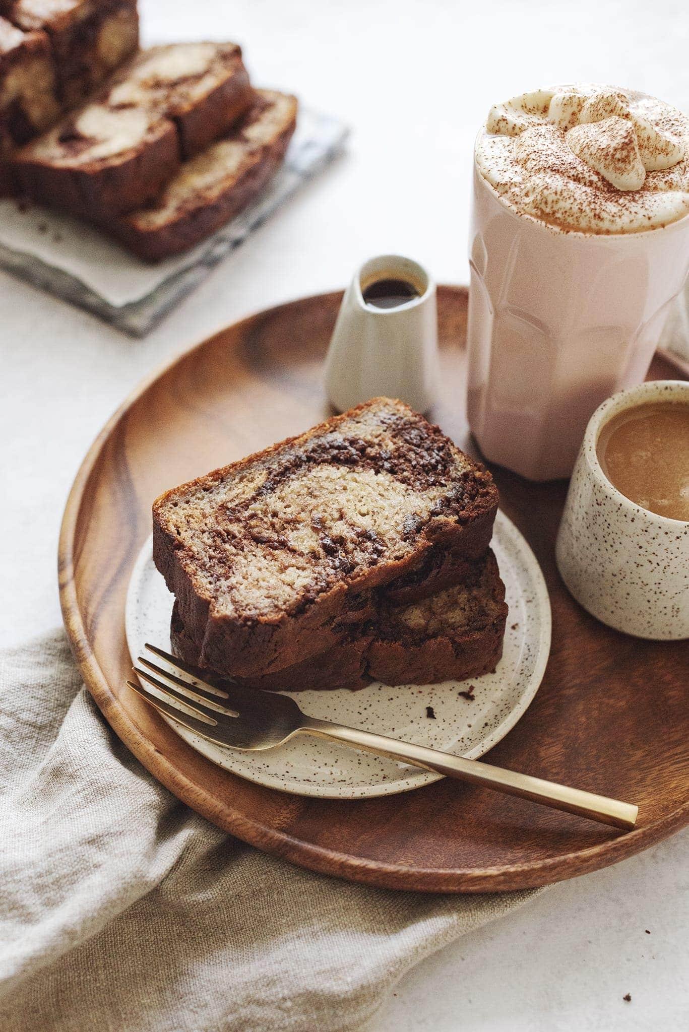slice of dark chocolate swirl banana bread on a rustic wooden board, steaming coffee