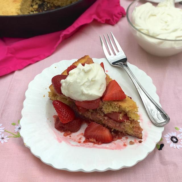A hand cutting a slice of strawberry shortcake cornbread