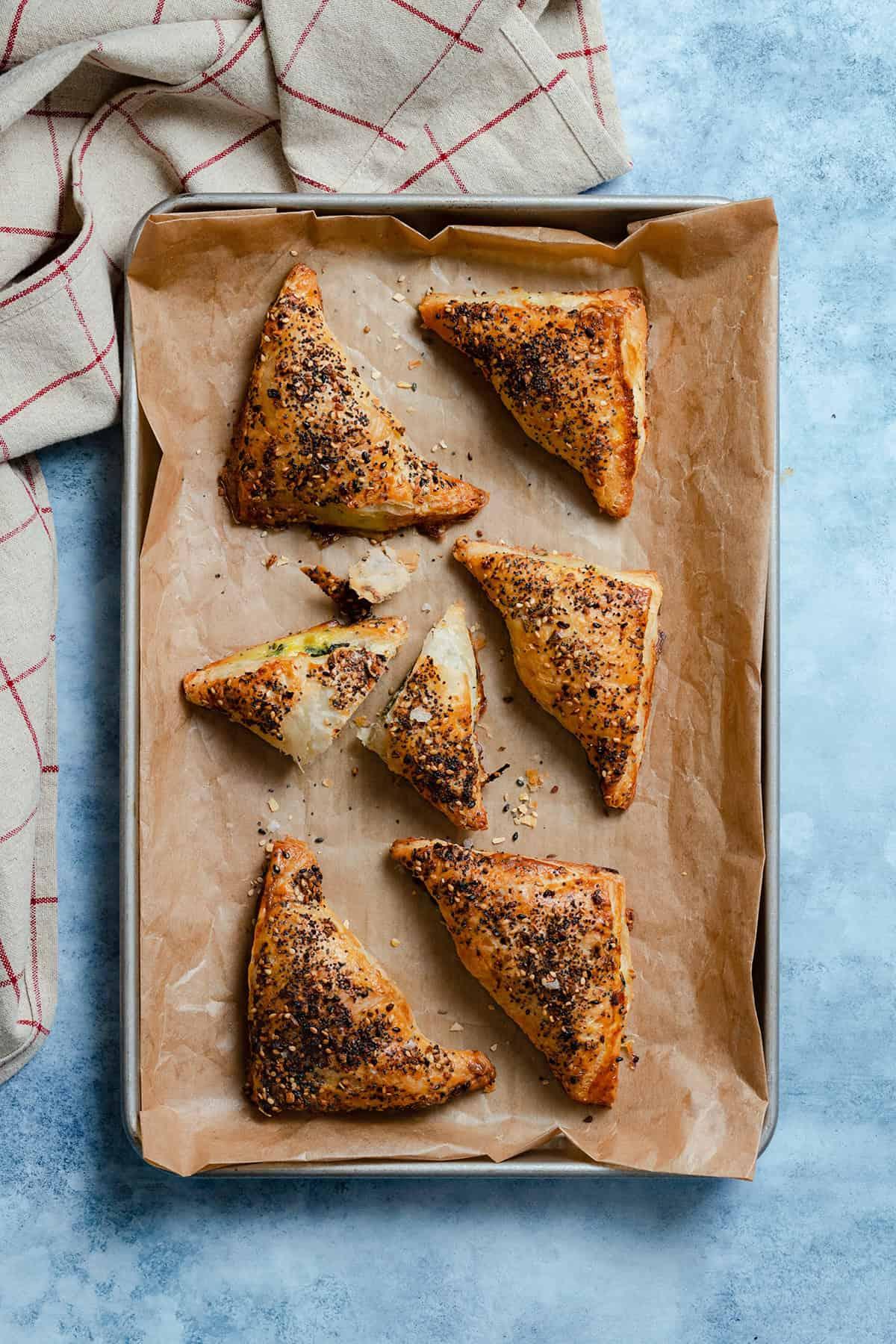 Overhead shot of freshly baked spinach feta pastry triangles on parchment paper, ready to be served
