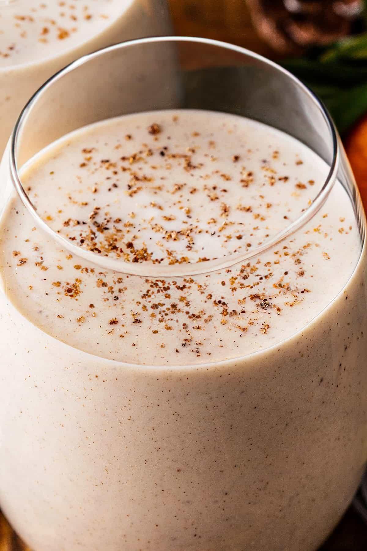 Close-up of freshly grated nutmeg and cinnamon sticks next to a glass of coquito