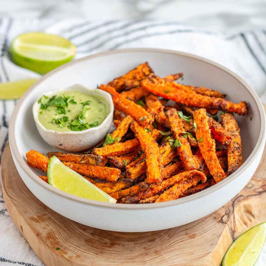 a tray of freshly baked carrot fries, golden brown and crispy, with a small bowl of avocado ranch dip alongside