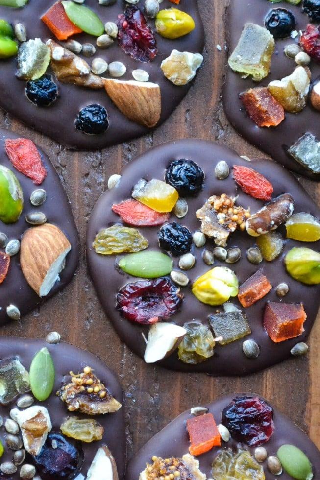 colorful dark chocolate mendiants with various dried fruits and nuts on parchment paper