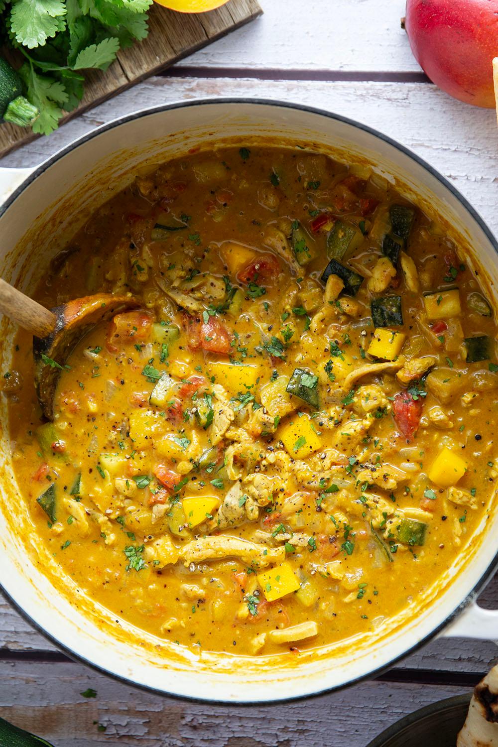 Close-up shot of chicken and vegetables simmering in a creamy curry sauce in a pot