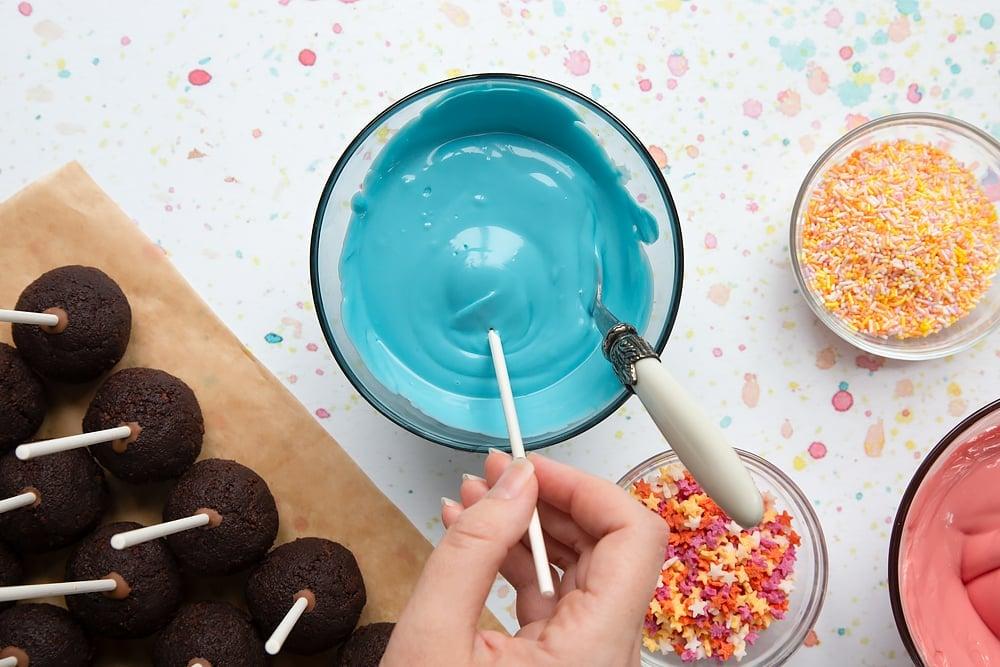 overhead shot of a person dipping a cake pop into melted chocolate