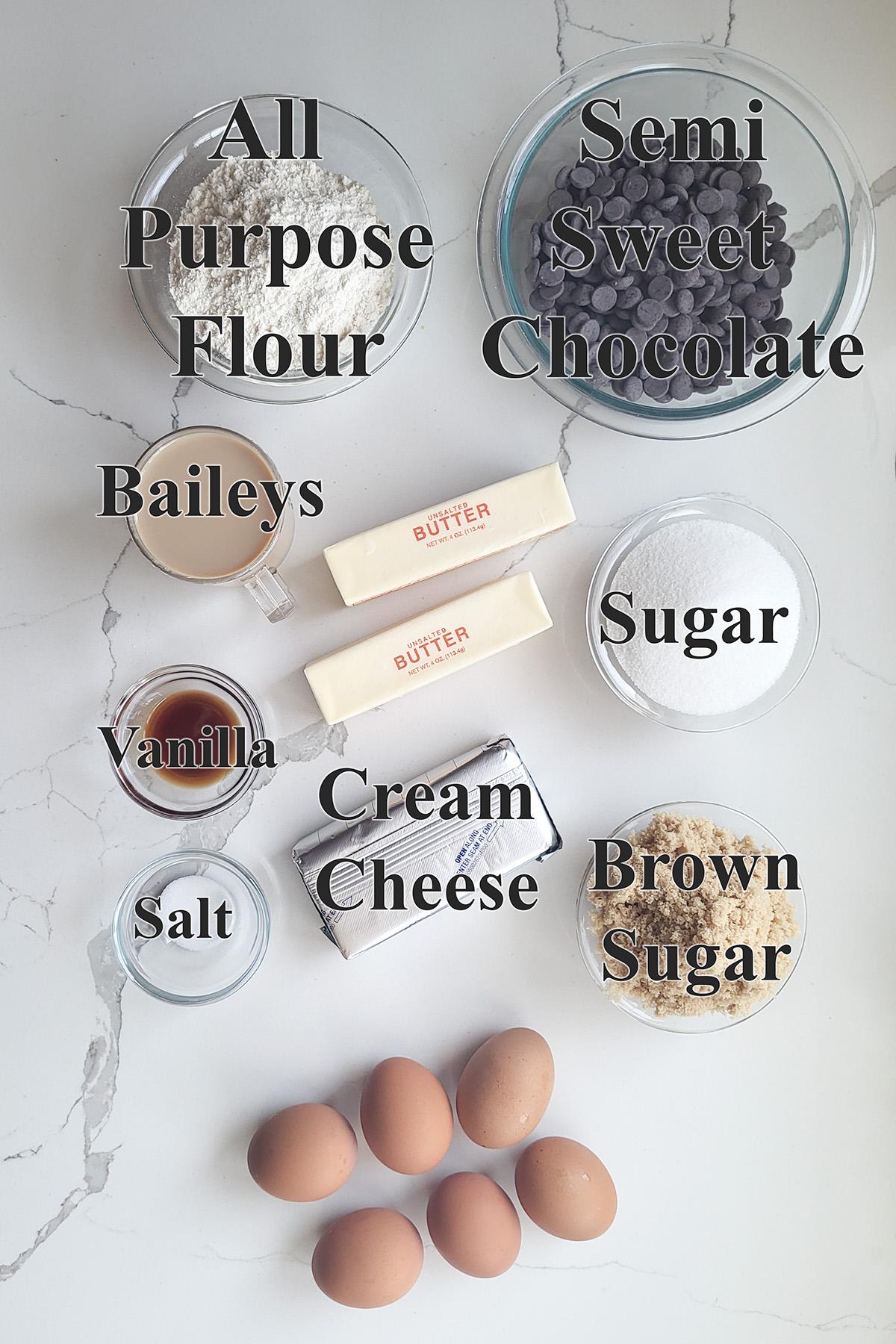 Ingredients for Baileys brownies arranged on a countertop, including chocolate, butter, sugar, eggs, flour, and Baileys Irish Cream.