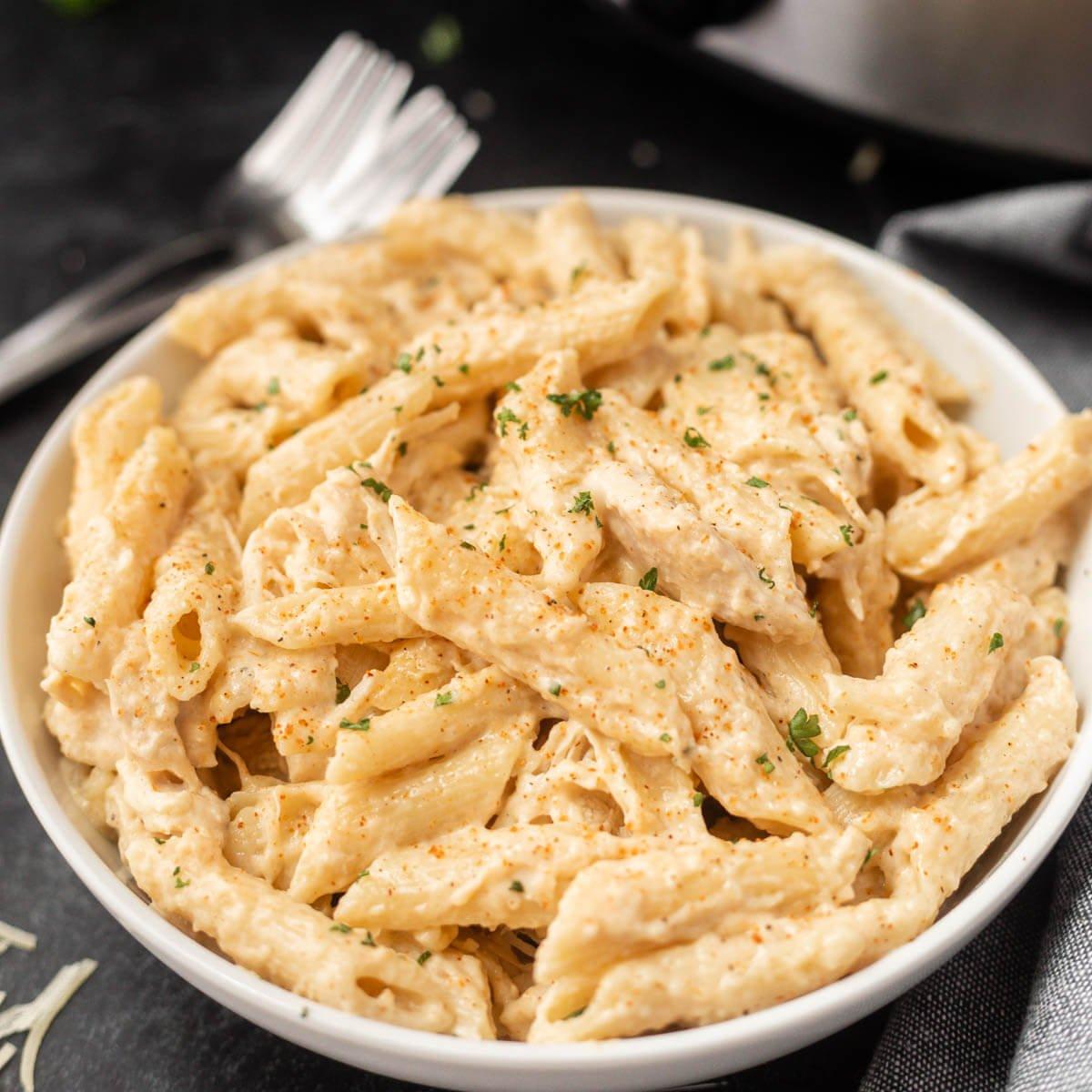 Creamy Cajun chicken pasta cooking in a crock pot, garnished with fresh parsley