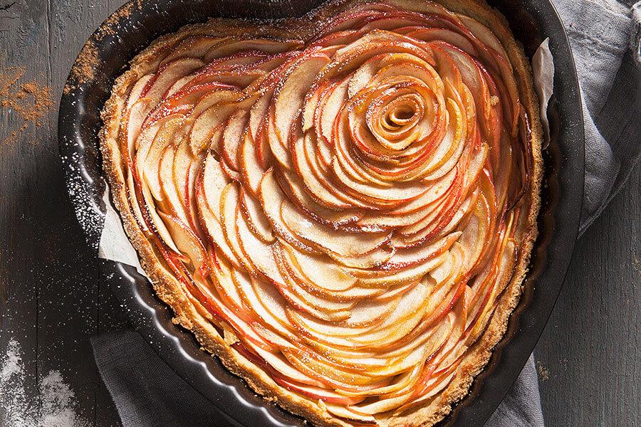 the completed bleeding heart apple tart served on a rustic wooden board with a dusting of powdered sugar