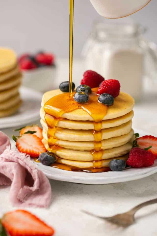 stack of fluffy grain-free gluten-free pancakes topped with fresh berries and maple syrup