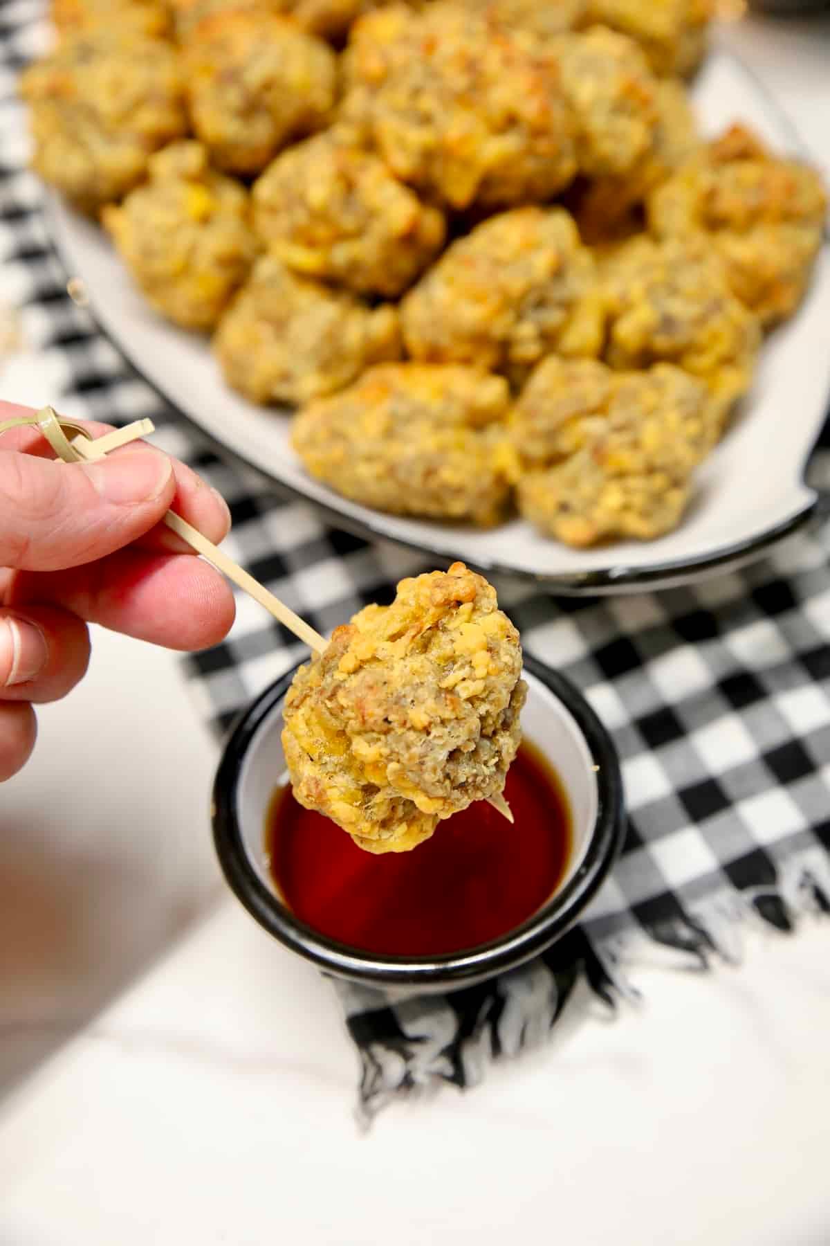 Hand drizzling maple hot sauce glaze over freshly baked sausage balls on a cooling rack