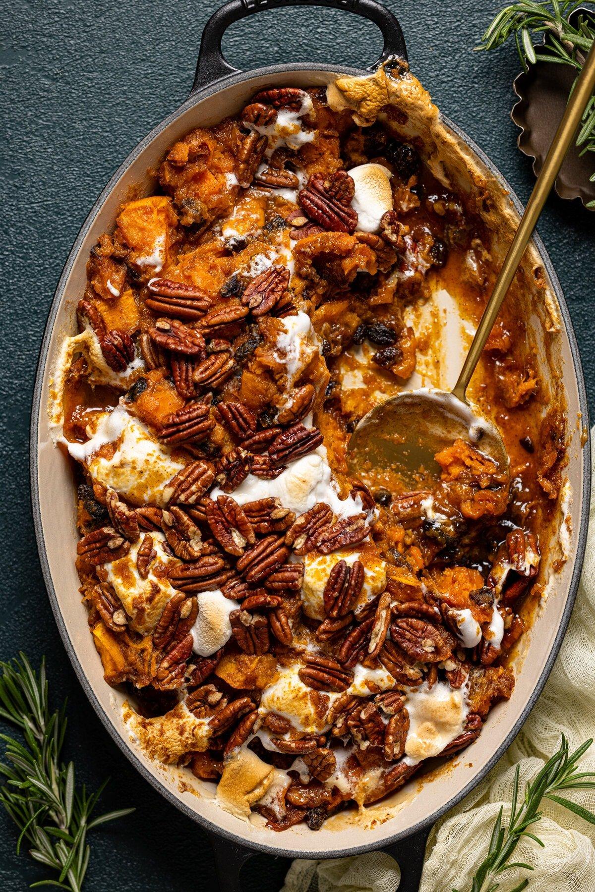 Vibrant sweet potato casserole with golden brown marshmallows and a maple butter drizzle on a rustic wooden table, garnished with a sprig of rosemary, cozy holiday lighting in background