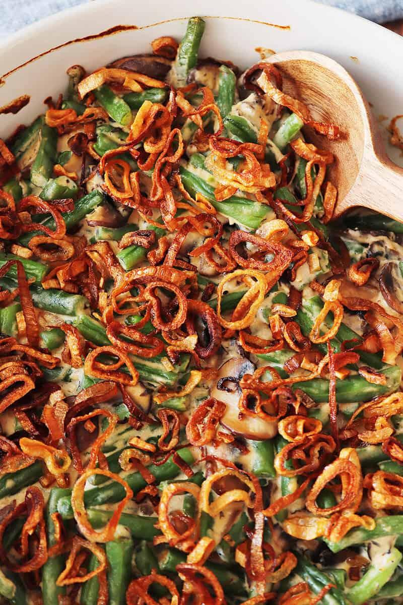 Close-up of a bubbling skillet green bean casserole with golden brown crispy topping and fresh herbs, rustic kitchen setting