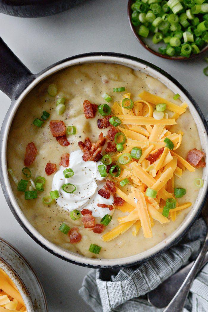 comforting potato soup bowl with crispy bacon bits and fresh green scallions on top, rustic setting