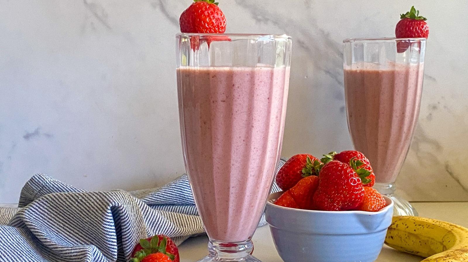 strawberry cinnamon smoothie in a glass with cinnamon sticks and fresh strawberries around it