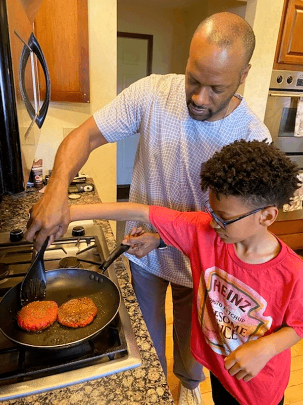 a dad cooking burgers on a griddle with kids around