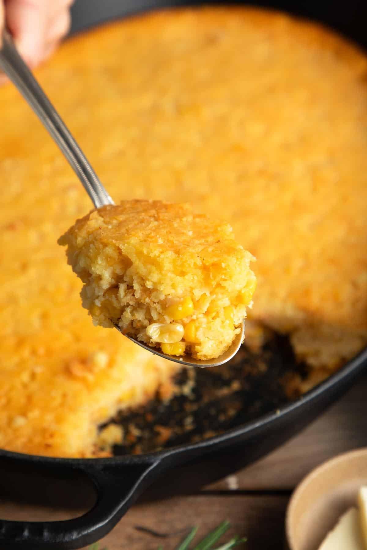 golden brown creamy corn casserole baking dish with a serving spoon, close-up, rustic kitchen setting