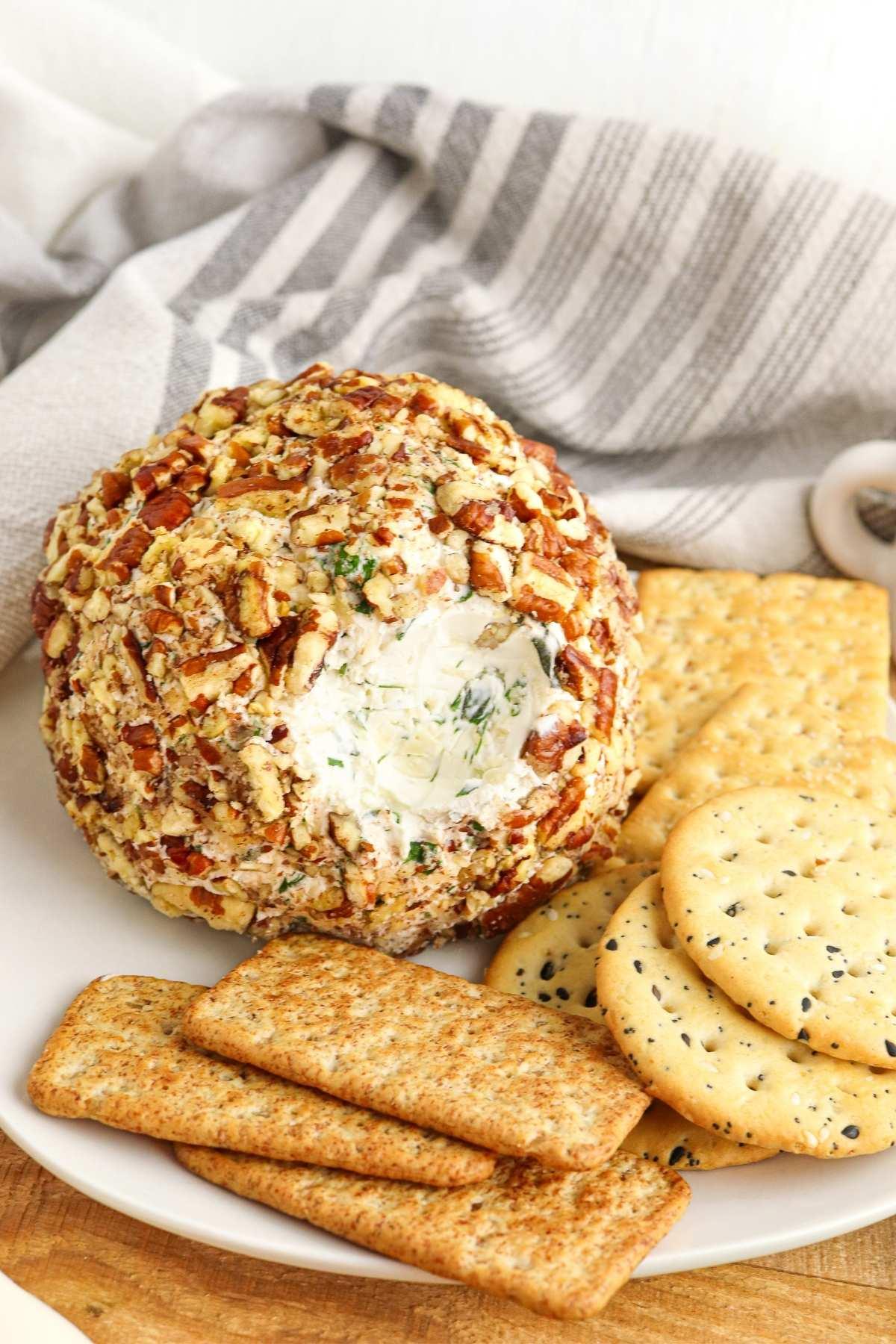 beautifully presented herbed cheese ball with a nut crust on a wooden board with crackers