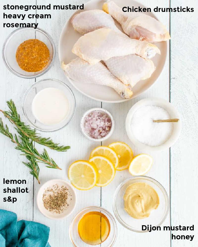 overhead shot of uncooked chicken drumsticks marinating in a bowl with lemon slices and herbs