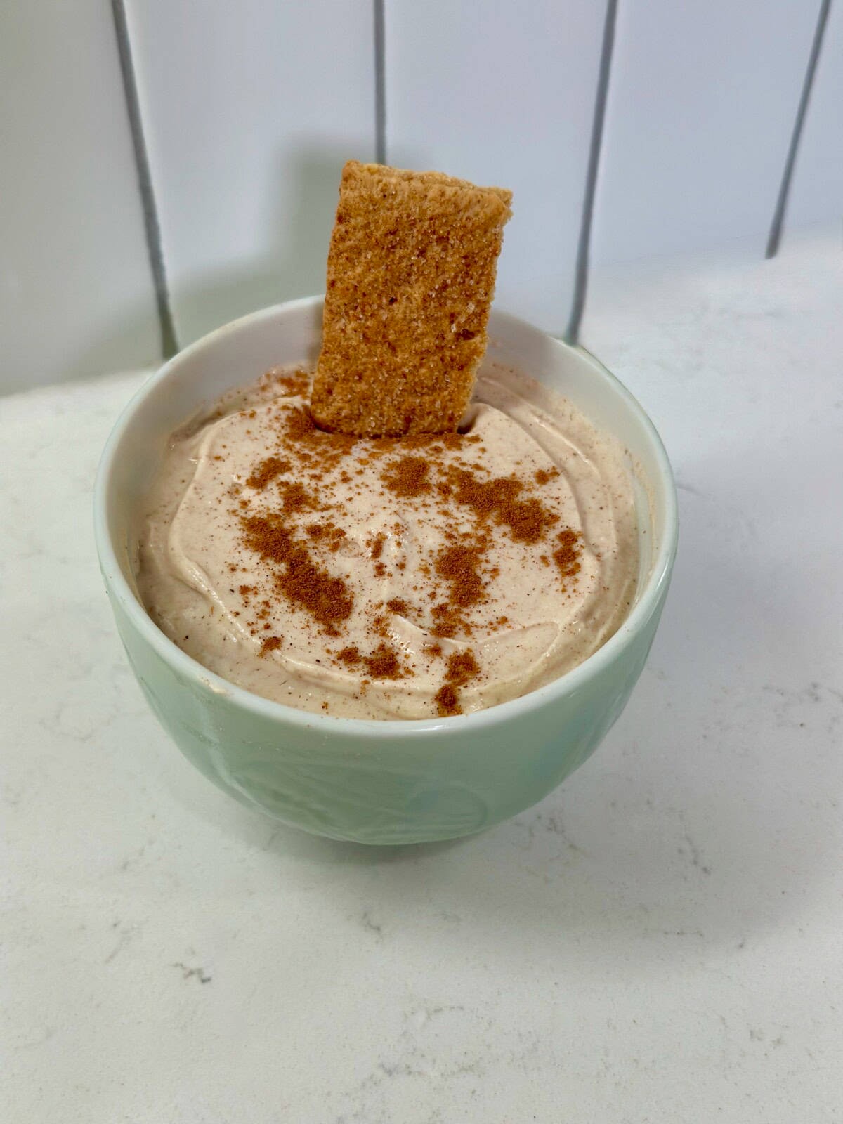 snickerdoodle cheesecake dip in a bowl with cinnamon sticks and graham crackers
