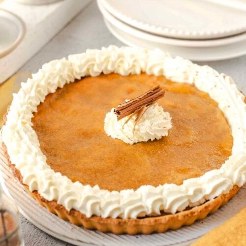 rustic homemade pumpkin pie with a generous whipped cream swirl, garnished with a sprinkle of cinnamon, cozy autumn background